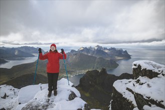 young woman in red jacket with hiking poles on snowy mountain