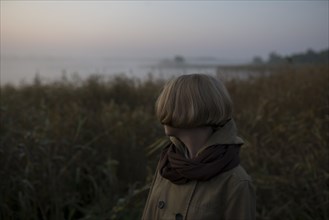 young woman in field by lake at sunset