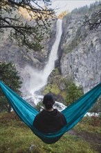 young man resting in hammock by waterfall