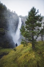 young man standing on hill by waterfall