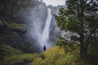 young man standing on hill by waterfall