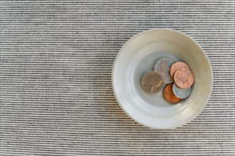 Bowl with small pile of coins on striped background