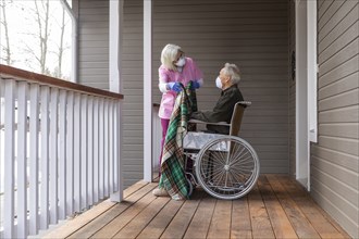 Woman and man in wheelchair wearing protective mask to prevent coronavirus transmission on porch