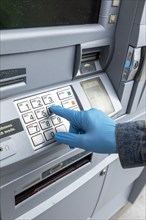 Close-up of gloved hand on keypad of ATM machine