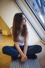 Young woman sitting on floor and looking through window