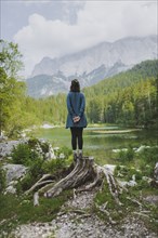 Germany, Bavaria, Eibsee, Young woman standing on stump by Frillensee lake in Bavarian Alps