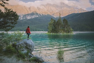 Germany, Bavaria, Eibsee, Young woman standing on rock by Eibsee lake in Bavarian Alps