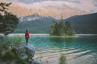 Germany, Bavaria, Eibsee, Young woman standing on rock by Eibsee lake in Bavarian Alps