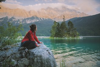 Germany, Bavaria, Eibsee, Young woman sitting on rock and looking at scenic view by Eibsee lake in Bavarian Alps