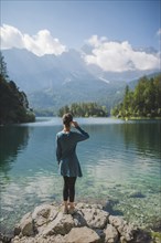 Germany, Bavaria, Eibsee, Young woman standing on rock at shore of Eibsee lake in Bavarian Alps