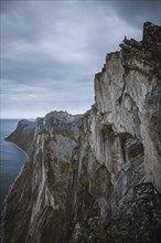 Norway, Senja, Man sitting on the edge of steep cliff on top of Segla mountain