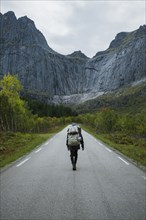Norway, Lofoten Islands, Backpacker walking down road in mountain landscape