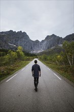 Norway, Lofoten Islands, Man walking down road in mountain landscape