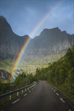 Norway, Lofoten Islands, Rainbow above empty road in mountain landscape