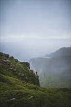 Norway, Lofoten Islands, Reine, Man looking at view from Reinebringen mountain during rain