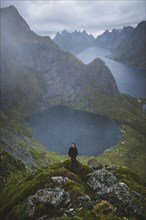 Norway, Lofoten Islands, Reine, Man on Reinebringen mountain with lake and fjord in background