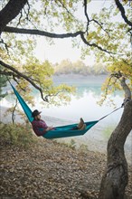 Italy, Man lying in hammock near lake