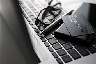 Credit card, smart phone, pen and glasses on laptop keyboard