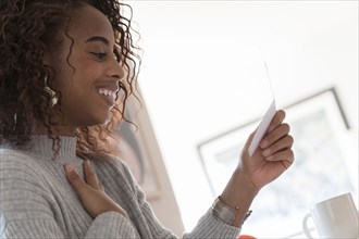 Smiling woman reading card touching her chest