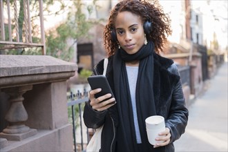 Woman wearing headphones holding smart phone and cup