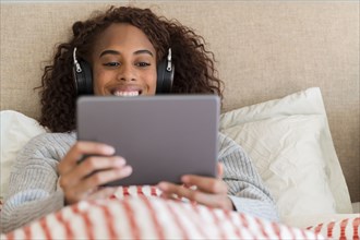 Smiling woman using tablet with headphones in bed