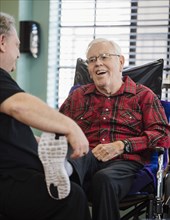 Nurse holding smiling senior man's foot in wheelchair