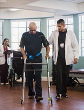 Doctor helping senior man use walking frame