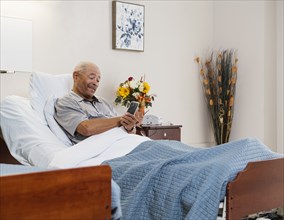 Senior man holding smart phone and flowers in bed