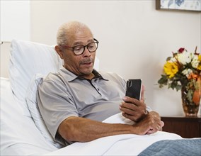 Senior man using smart phone in bed