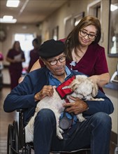 Smiling nurse pushing senior man holding dog in wheelchair