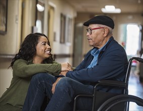 Smiling woman kneeling by senior man in wheelchair