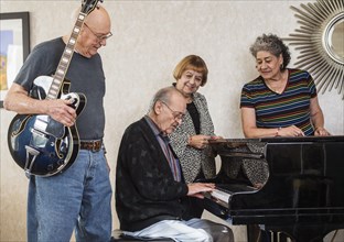 Senior people watching senior man playing piano