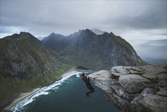 Man hanging off cliff at Ryten mountain in Lofoten Islands, Norway