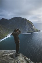 Man taking photograph on cliff at Ryten mountain in Lofoten Islands, Norway