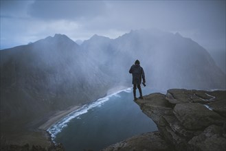 Man holding camera on cliff at Ryten mountain in Lofoten Islands, Norway