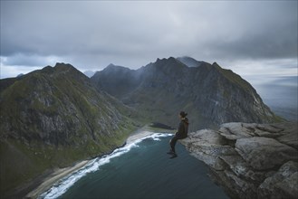 Man sitting on cliff at Ryten mountain in Lofoten Islands, Norway