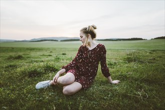 Blonde woman wearing dress sitting in field