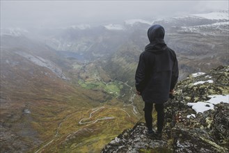 Man holding camera on Dalsnibba mountain overlooking valley in Geiranger, Norway