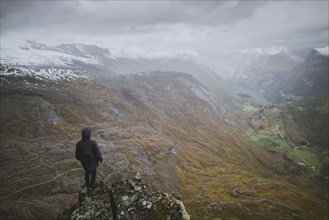 Man standing on Dalsnibba mountain overlooking valley in Geiranger, Norway