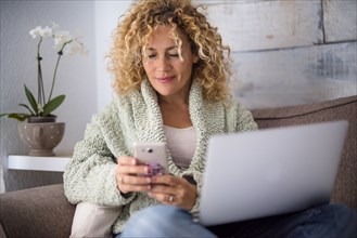 Smiling woman using smart phone and laptop on sofa