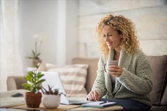 Smiling woman holding drink at laptop