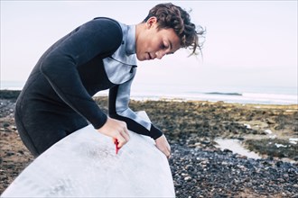 Teenage boy waxing surfboard at beach