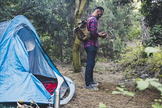 Man using smart phone by tent in forest