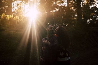 Smiling couple embracing by sunlight in forest