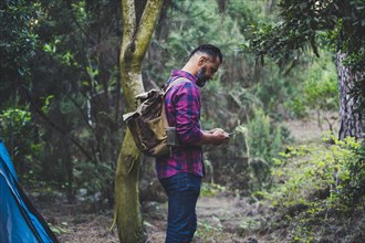 Man wearing backpack using smart phone in forest