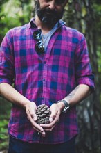 Man wearing checked shirt holding pinecone
