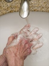 Senior woman washing hands in bathroom sink, close-up of hands