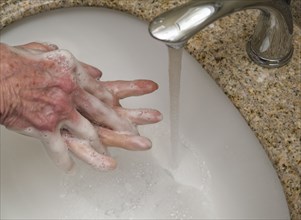 Senior woman washing hands in bathroom sink,  close-up of hands