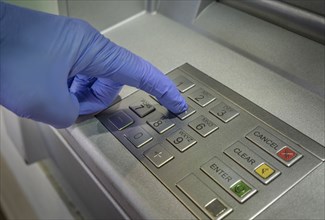 Gloved hand pushing button of cash machine