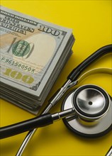 Stack of 100 dollar bills and stethoscope on yellow background